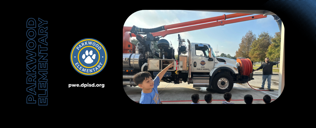 A student points towards a public service vehicle with a hose, with a school banner in the background.