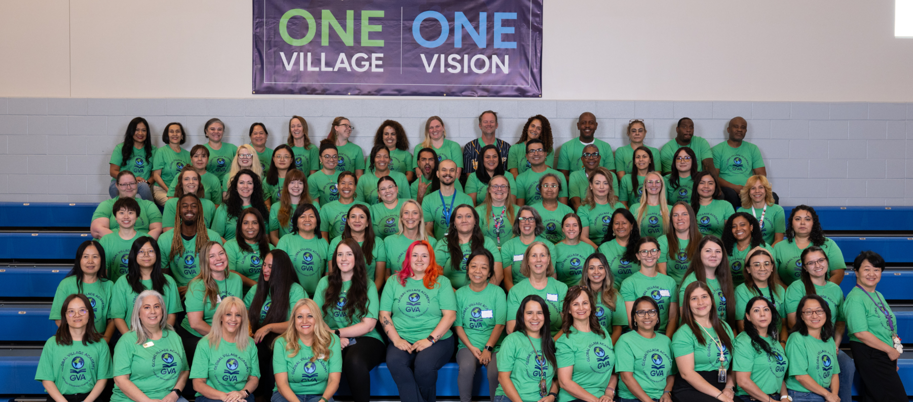 A large group of people wearing green shirts gathered in a gym, smiling for a photo.