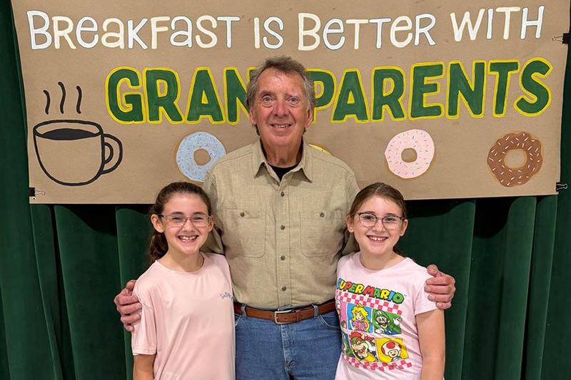a man stands between two girls with his arms around their shoulders
