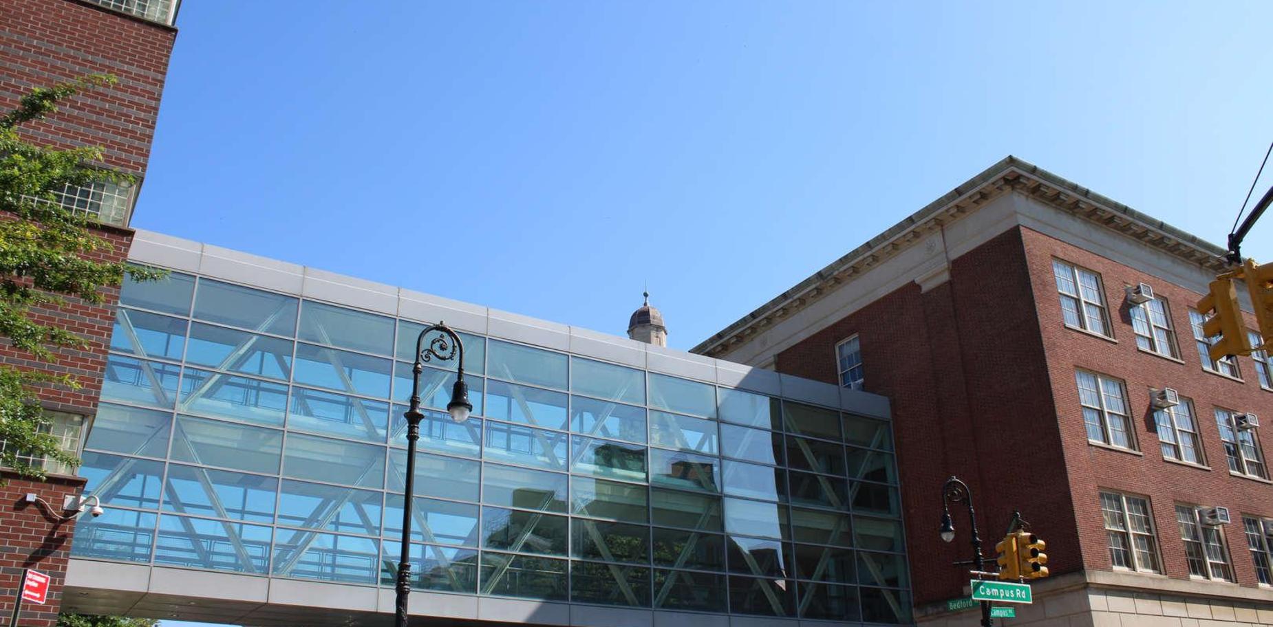 Modern glass walkway connecting two brick buildings under a clear blue sky.