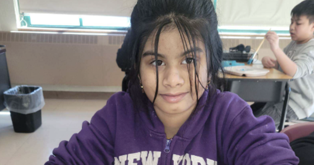 Child holding a paintbrush with pink paint, smiling while painting a crafted head.