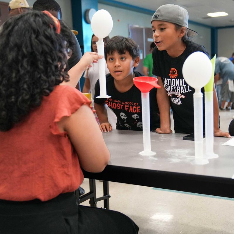 Students looking at science experiment with balloons and a cylinder tube.