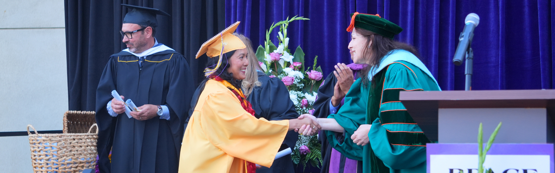 A graduate in a cap and gown shakes hands with Director during graduation.
