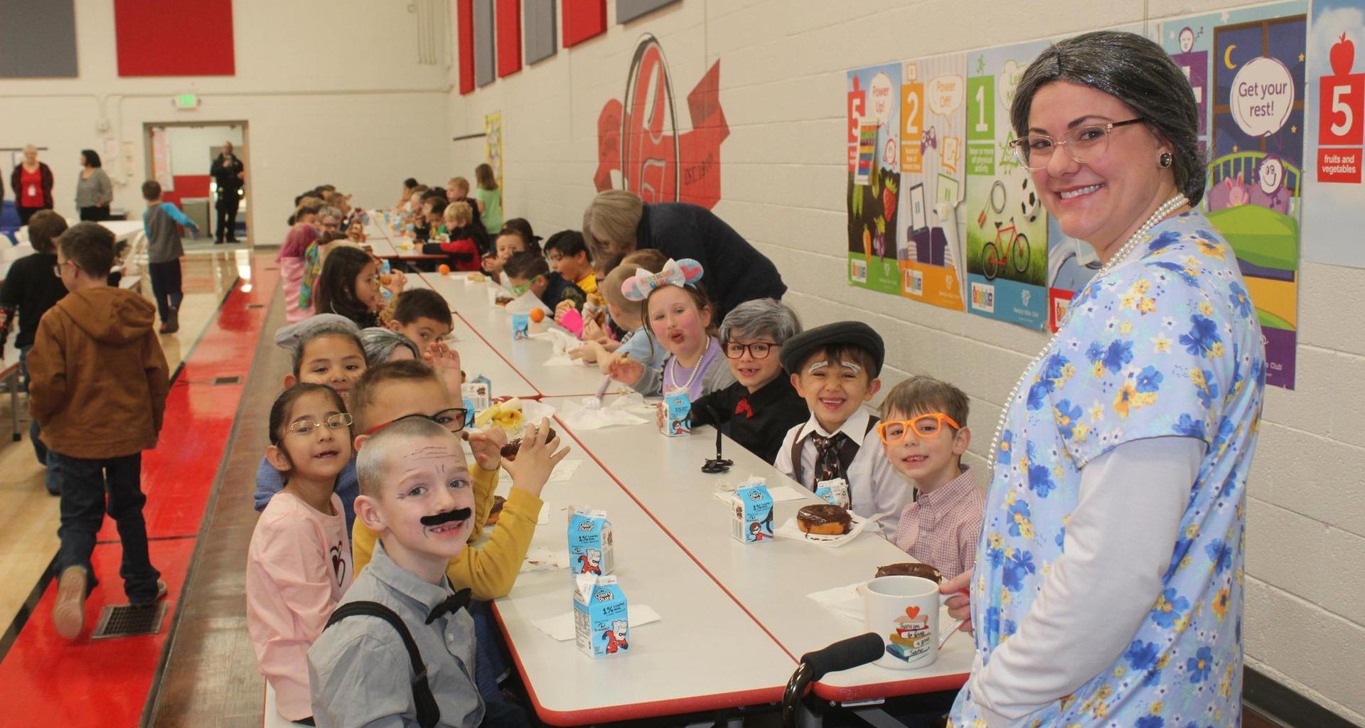 Students enjoying a meal in a school cafeteria, smiling at the camera.