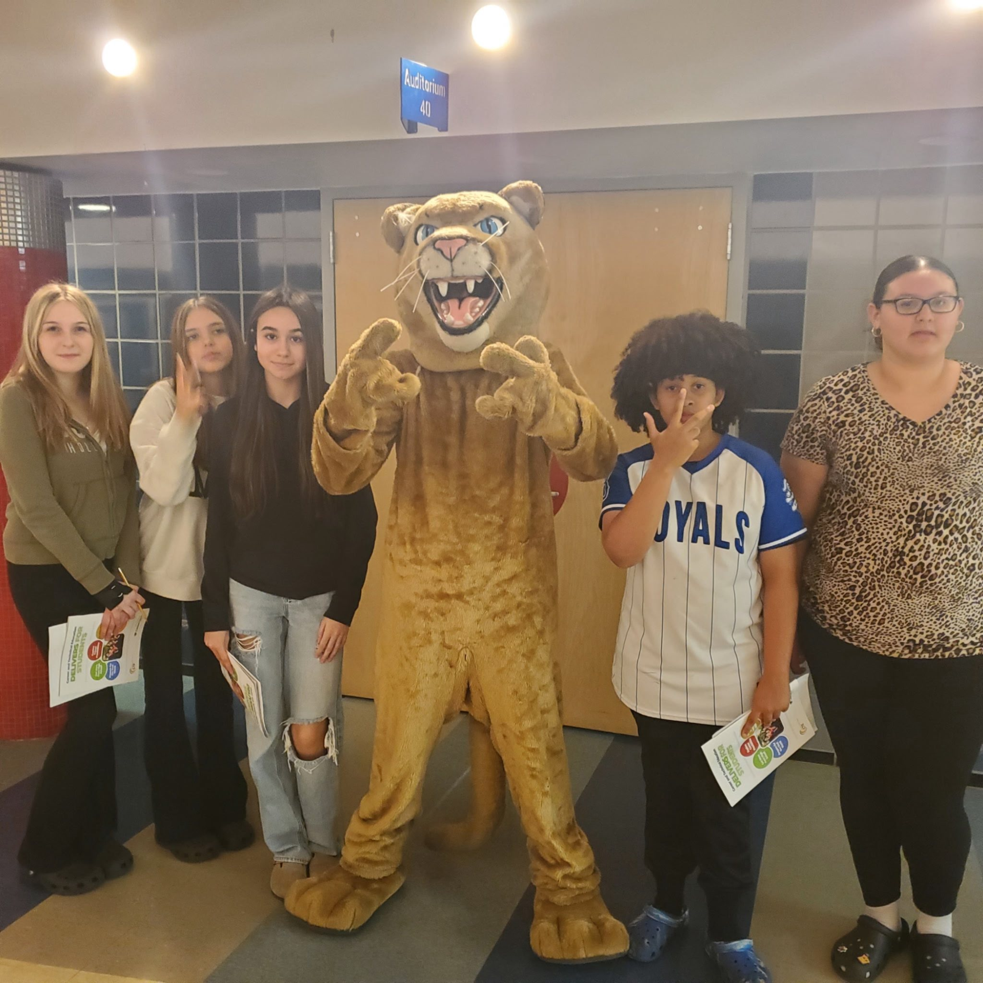 Group of students posing with a mascot in a school hallway.