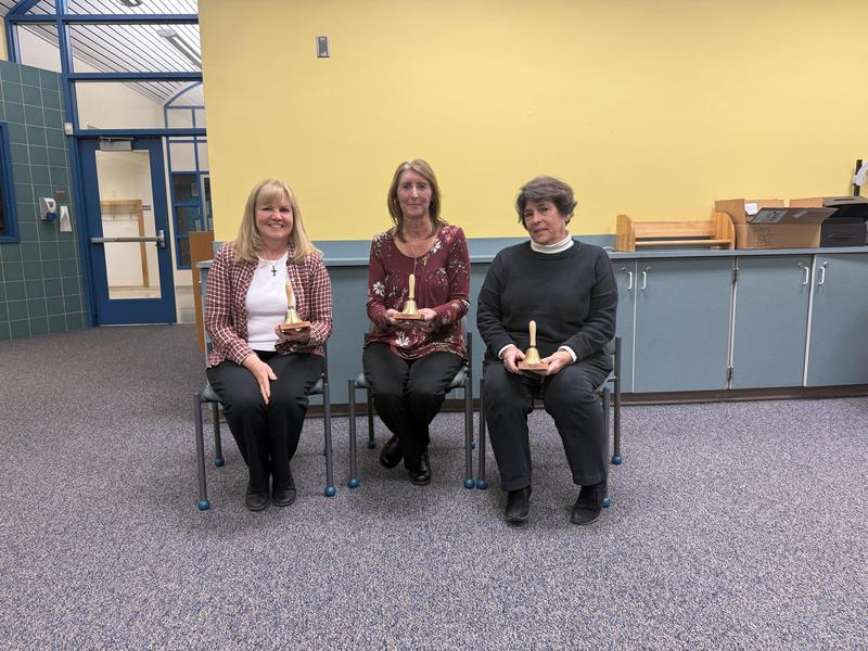 Three woman school board members seated holding bells they received