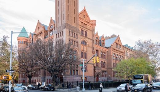 Scenic view of a grand historic building surrounded by trees and traffic on a city street.
