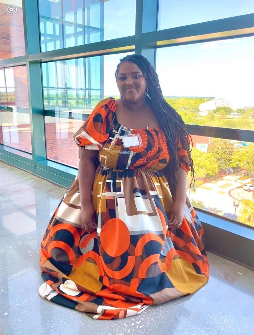 Woman in a colorful dress posing by a large window with a view.