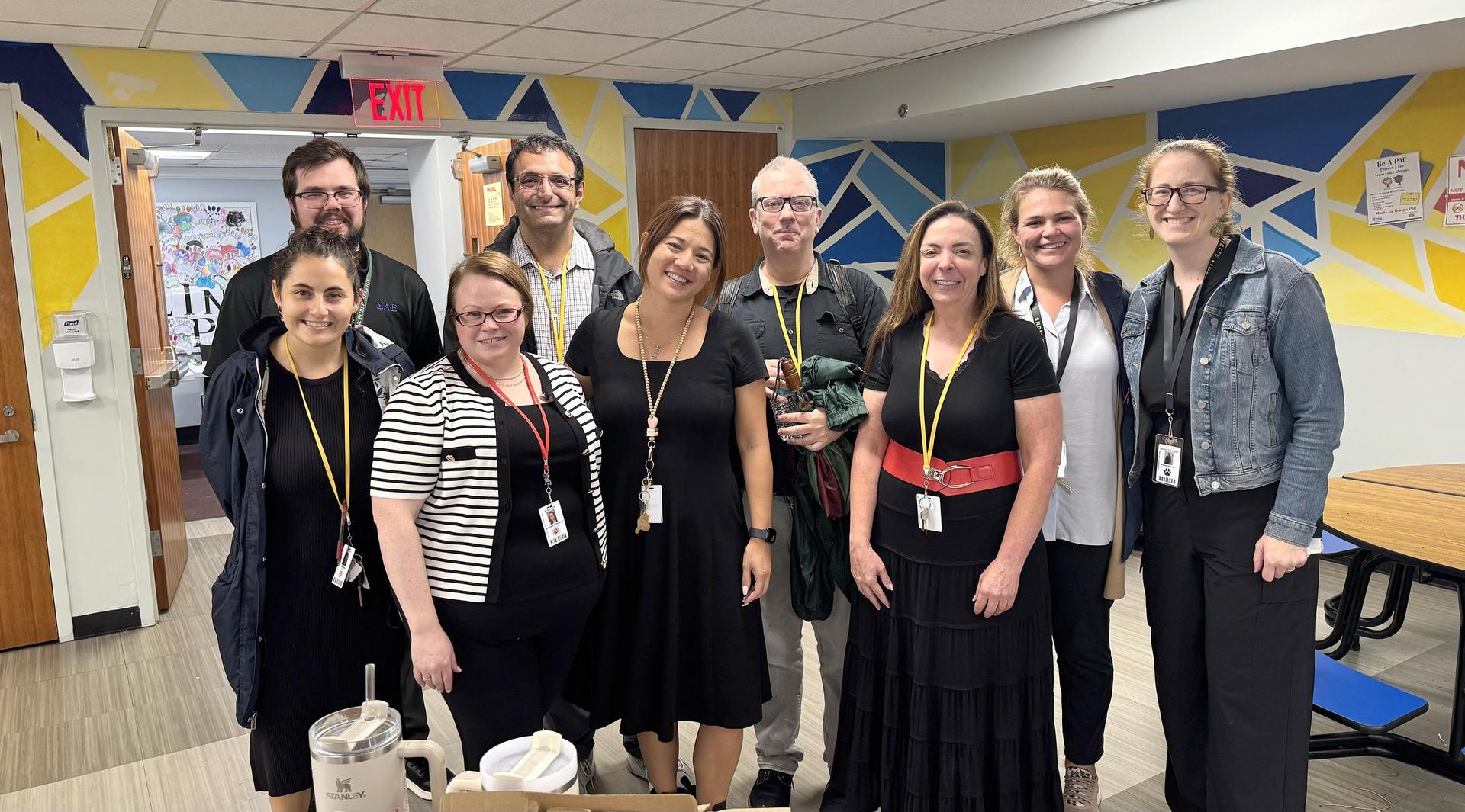 Group of eight adults standing together in a brightly colored room with backpacks in the background.