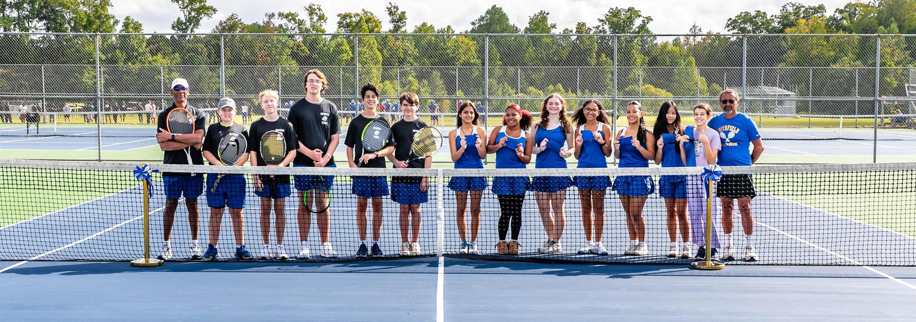 A group of young tennis players posing together on a court with their coaches.