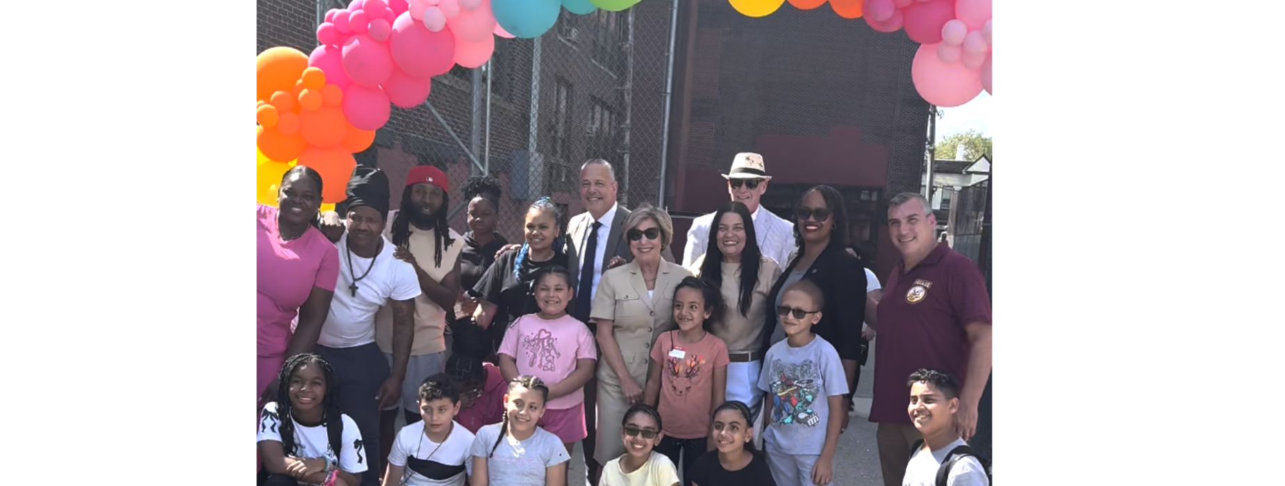 A diverse group of children and adults posing under a colorful balloon arch.
