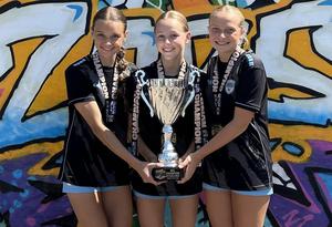 Three female soccer players holding a championship trophy