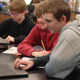 Three students collaborating at a desk with a laptop.