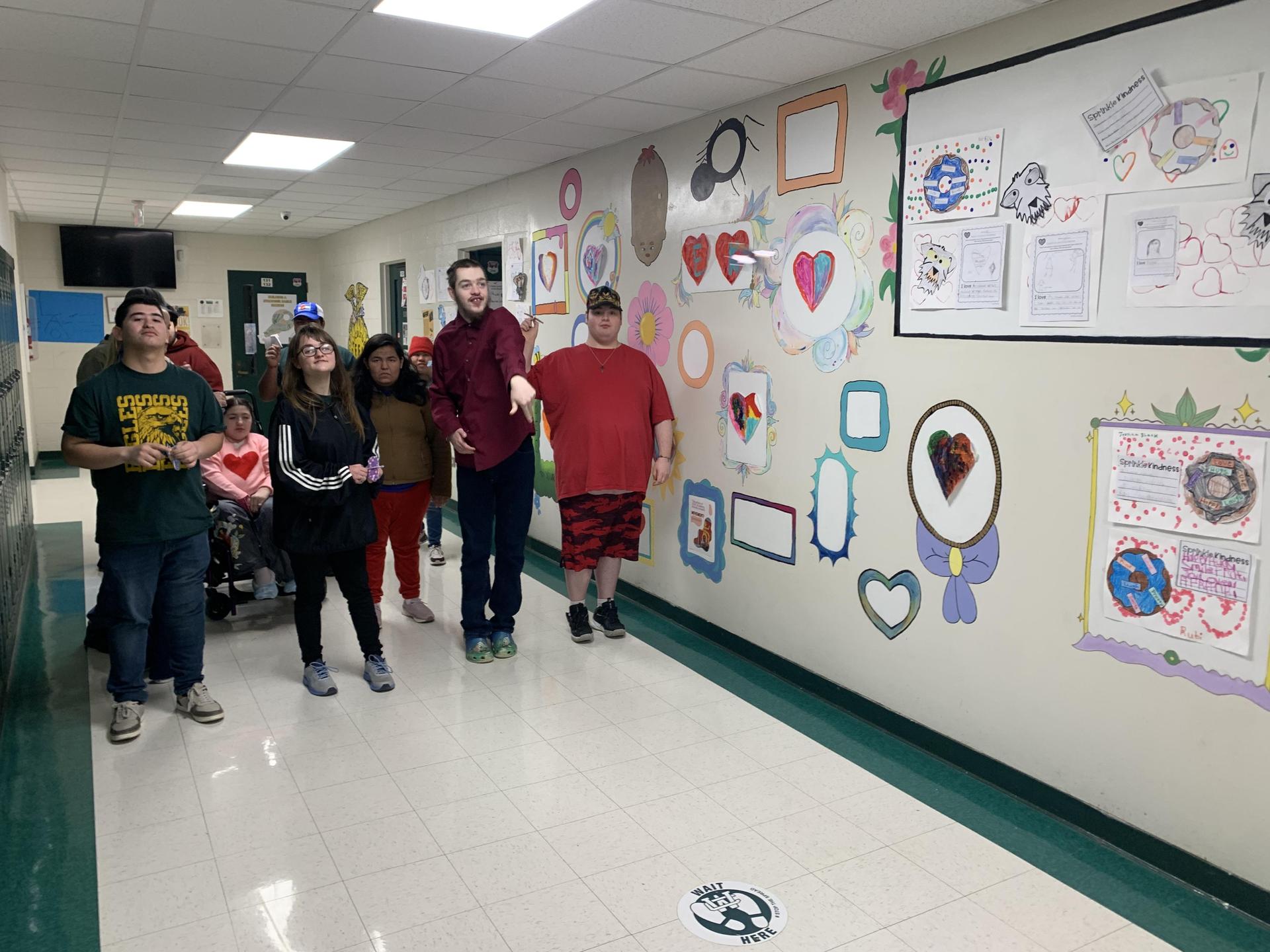 Students standing in a brightly decorated hallway with artwork on the walls.