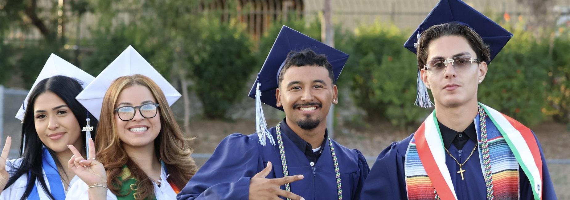 Group of four graduates in caps and gowns, celebrating with smiles.