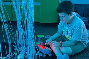 A student sits on the floor and is mesmerized by the hanging glow light and new toys to use while in the sensory room