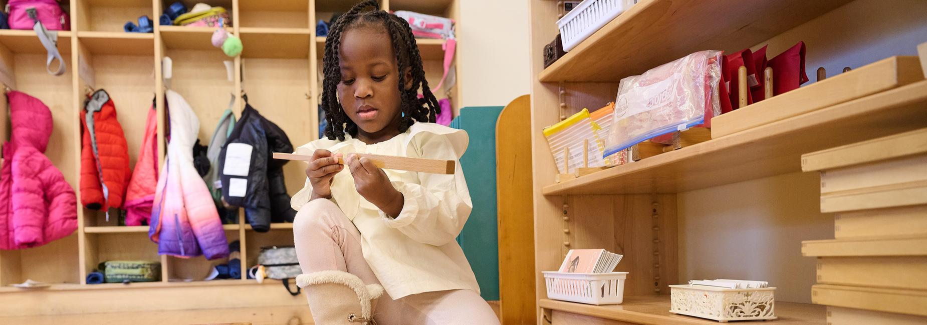 A child focused on building with wooden blocks while seated on a mat.