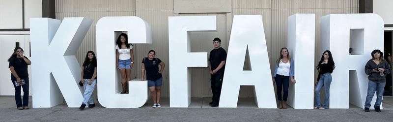 Group of people posing with large letters spelling 'KC FAIR'.