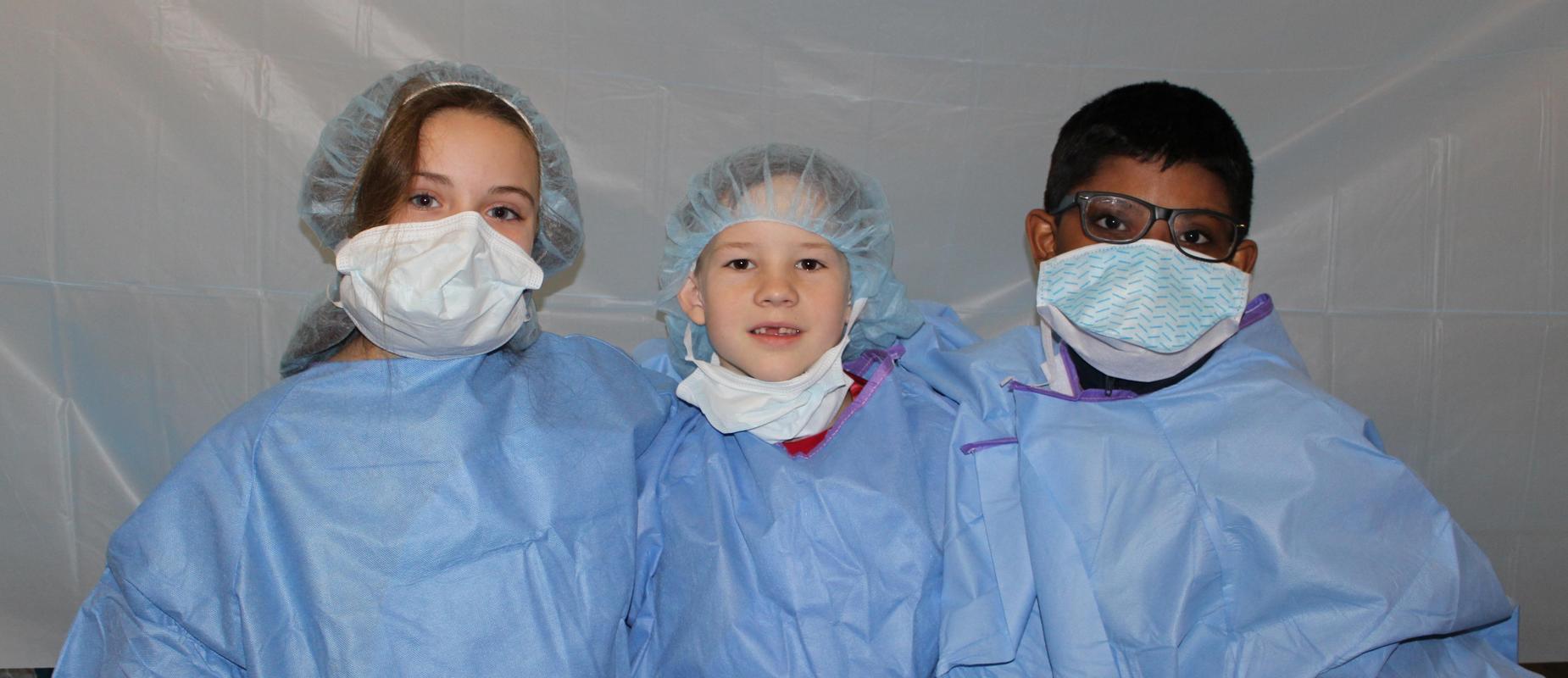 three third graders in hospital scrubs and masks
