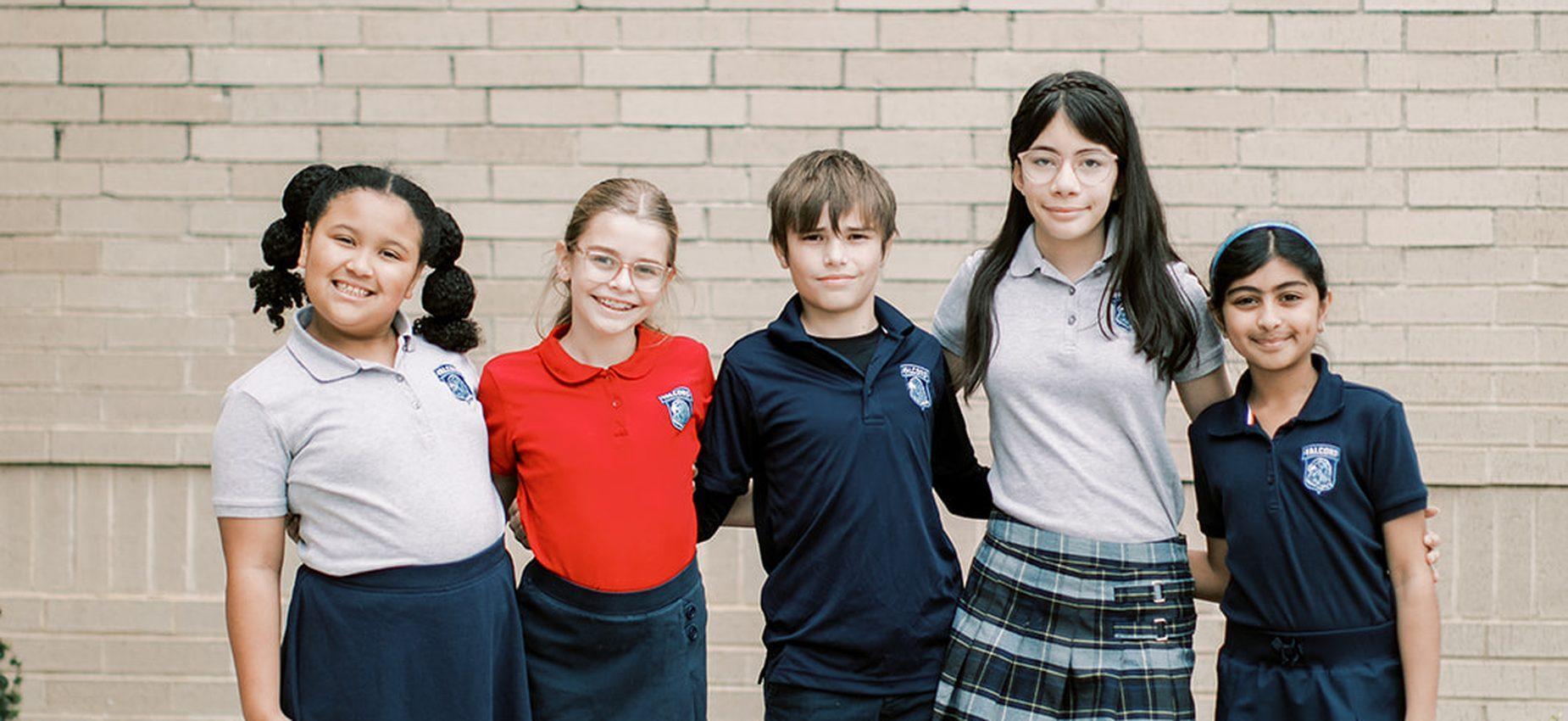 Five Coppell Classical Academy students in uniform smiling together by the school's brick wall