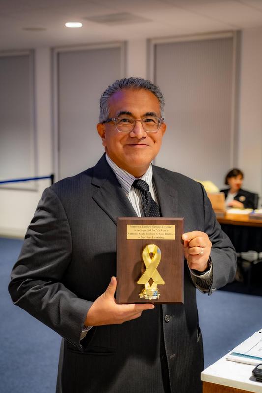 Mr Meza holding Blue ribbon plaque at board meeting