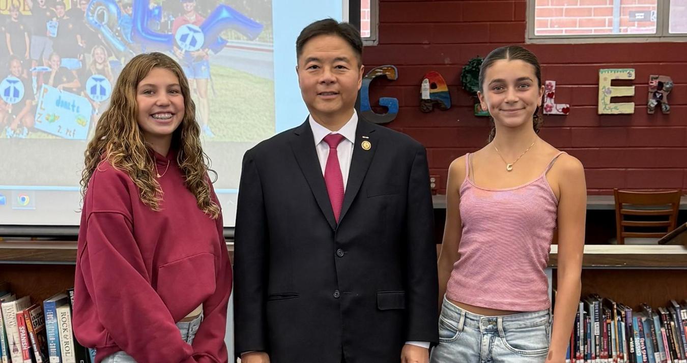 Two young women pose with a man in a suit in a library setting.