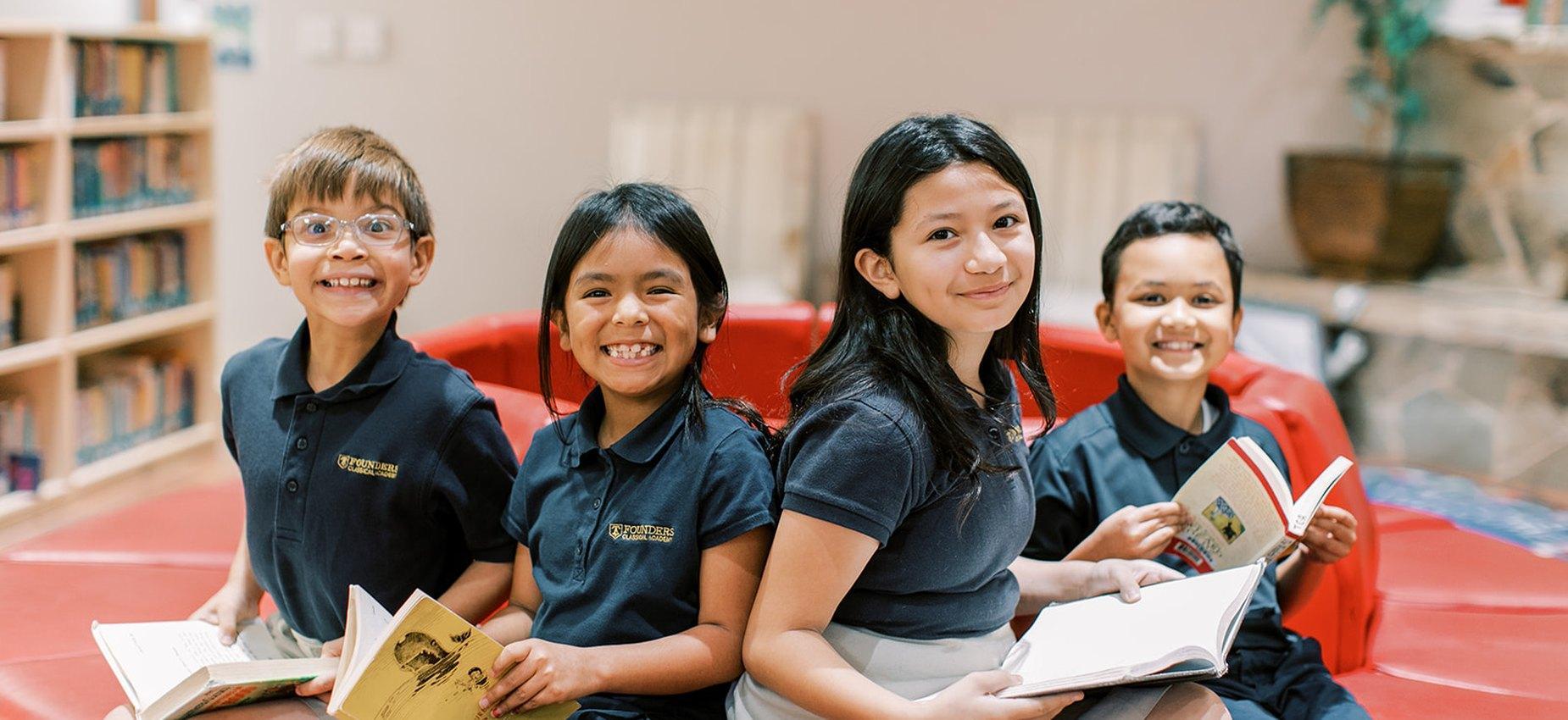 Four smiling Founders Classical Academy of Corinth students reading together on a library couch