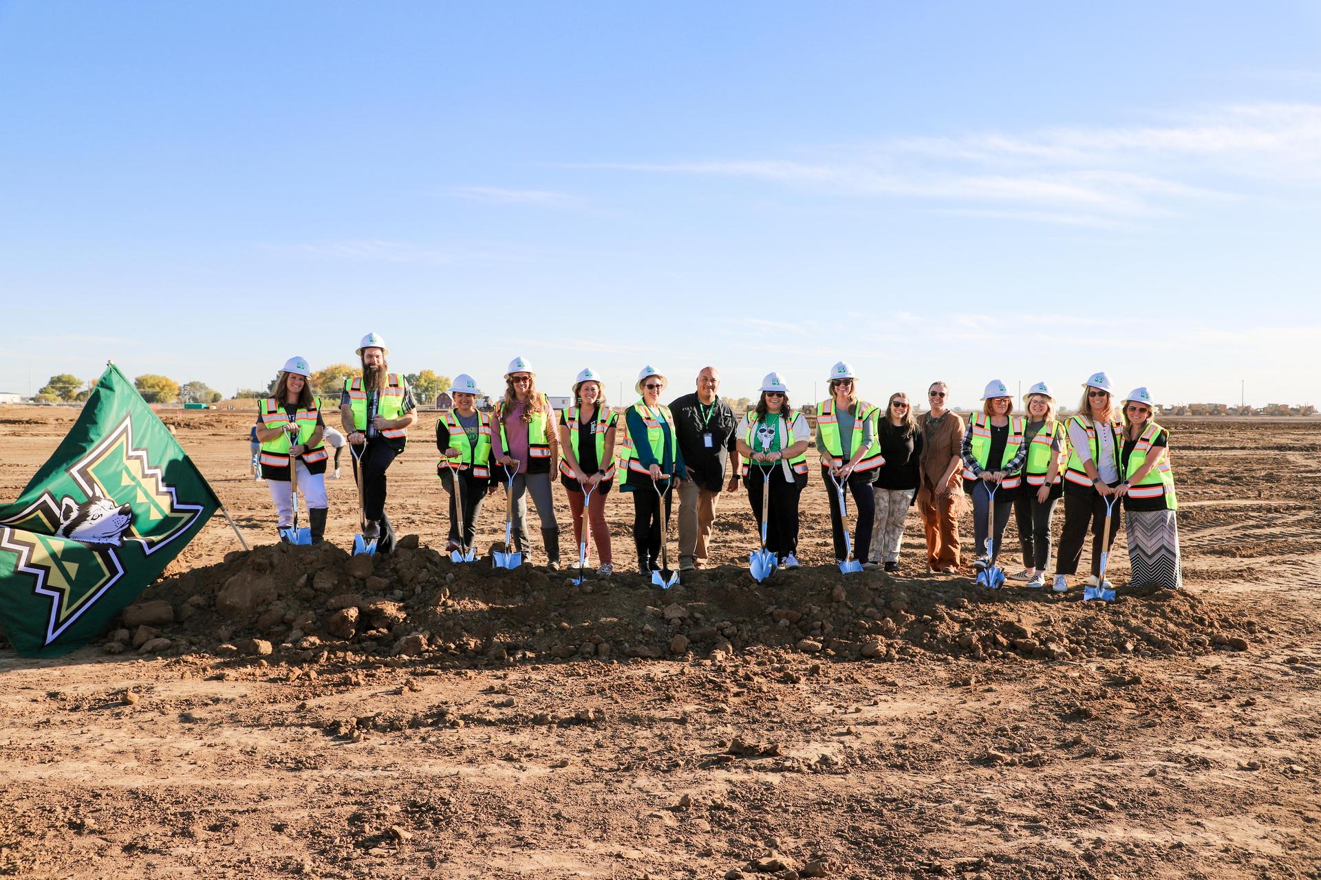 Large group in vests posing with a flag at a construction site.