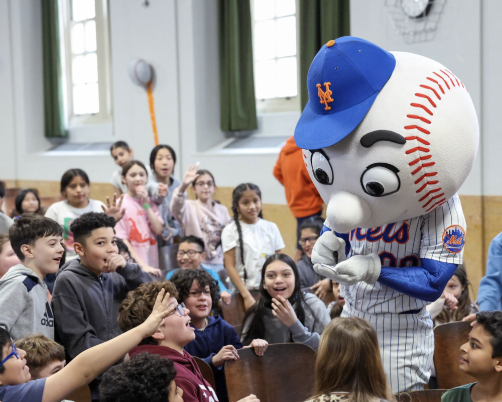 The NY Mets mascot in a baseball outfit interacting with excited children in a school setting.