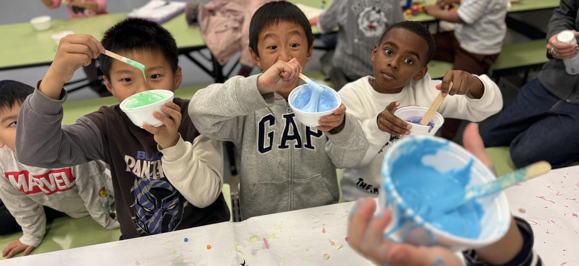 Three children joyfully mixing colorful paints in bowls during an art activity.