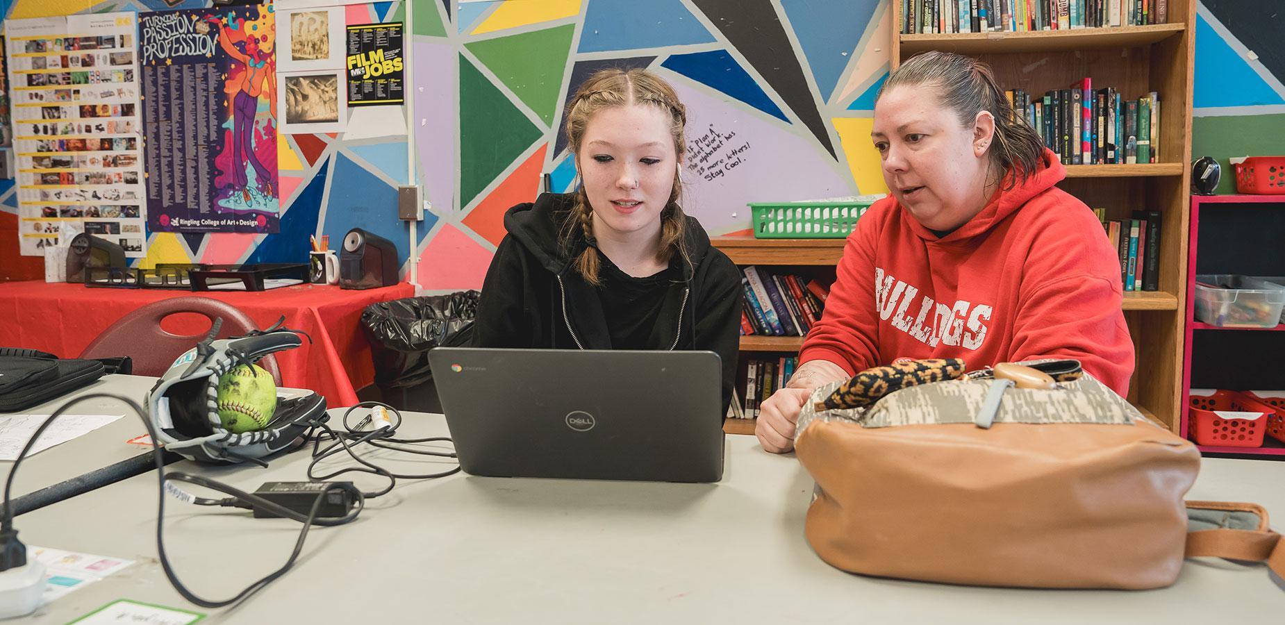 high school student looking at chromebook with teacher