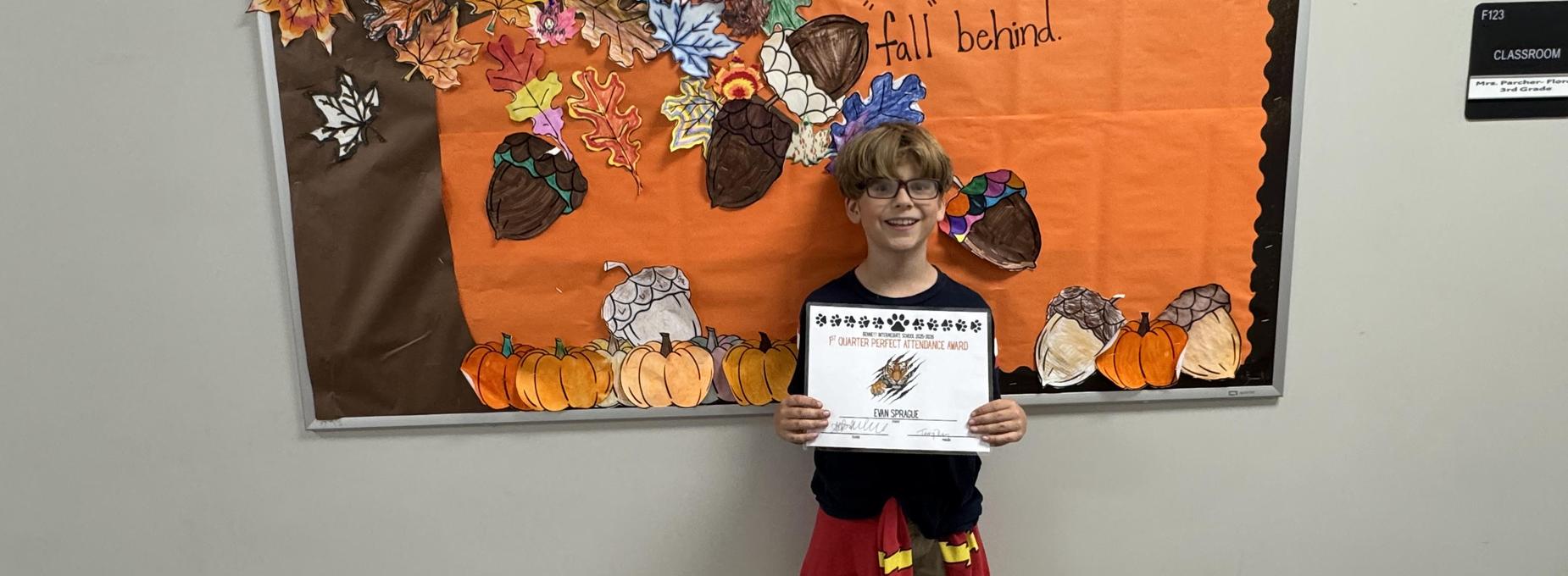 Child in glasses displaying a certificate against a fall-themed bulletin board.