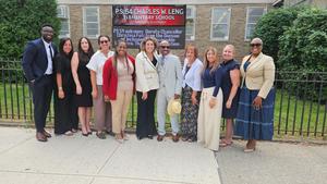 Group of educators standing in front of a school sign, smiling together.