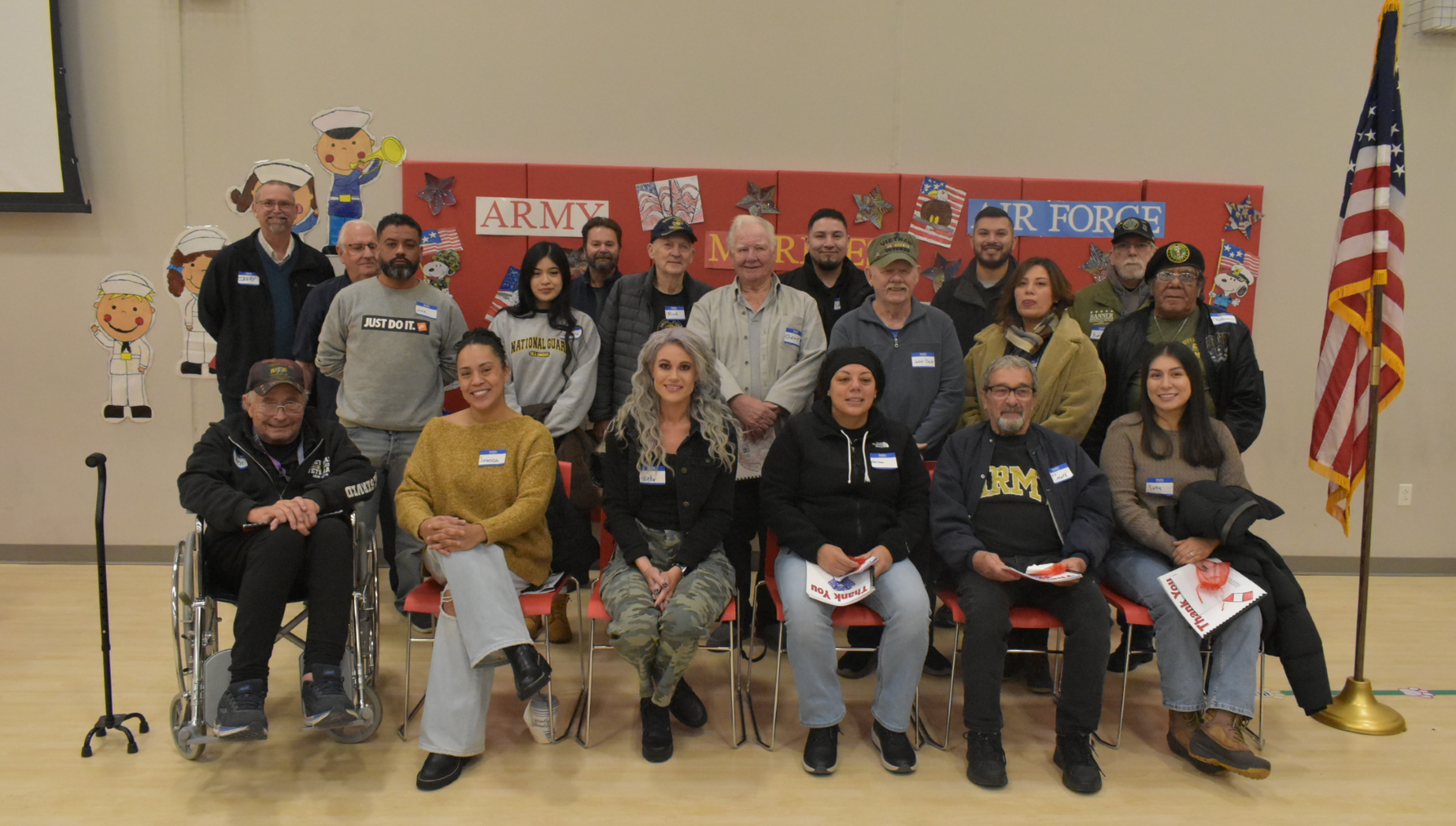 A group of military veterans sitting together, smiling, with decorations in the background.