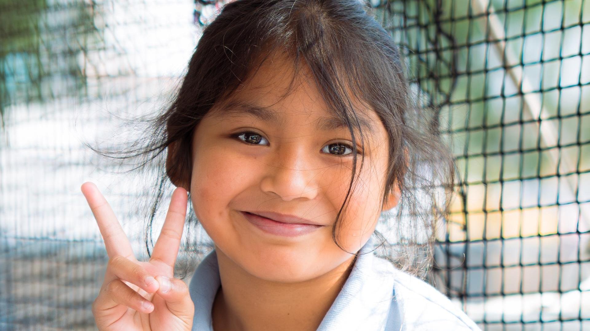 Smiling girl making a peace sign while posing for the camera.