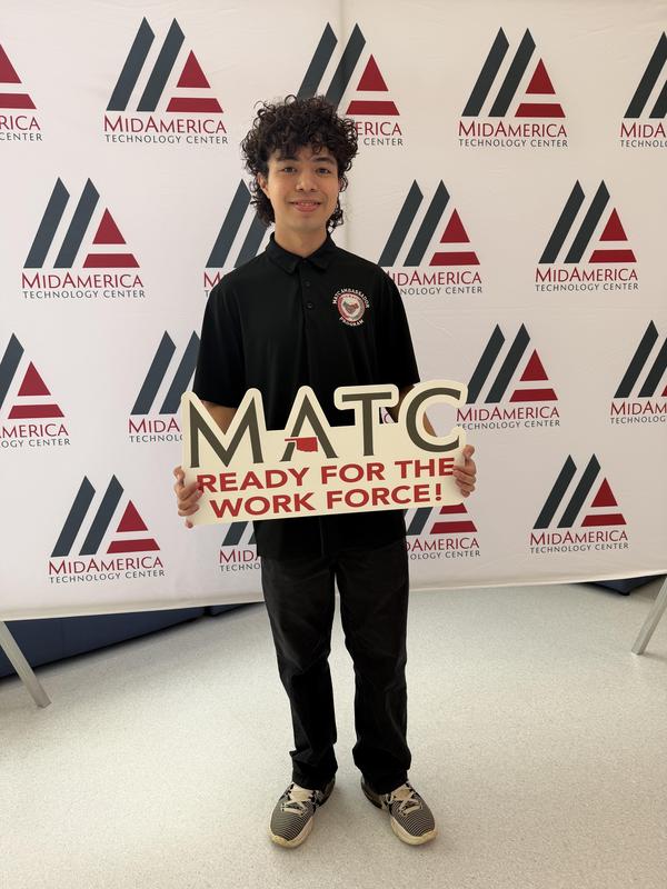 Student holds a sign with 'MATC READY FOR THE WORK FORCE' against a branded background.