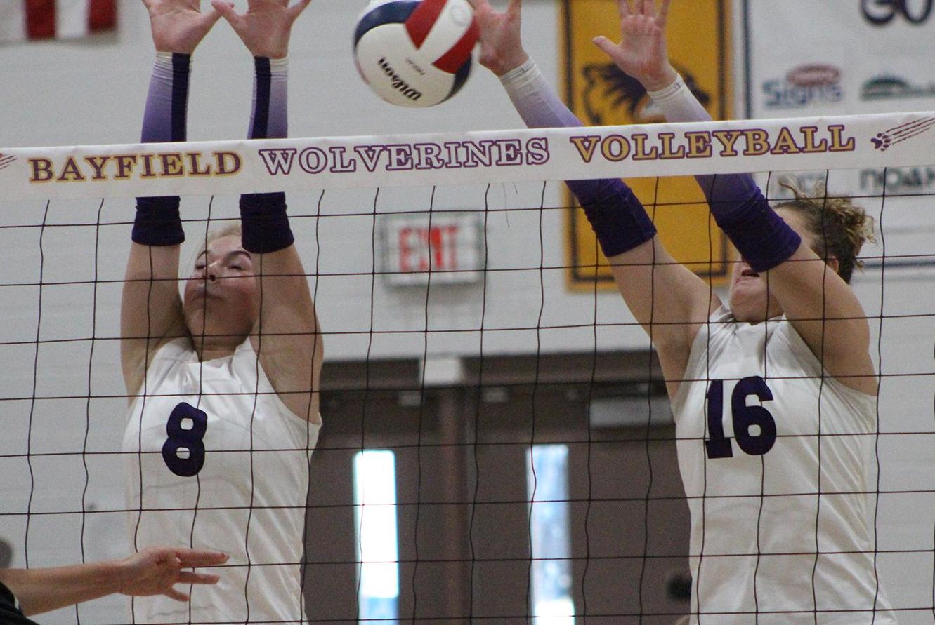 Two volleyball players make a block at the net.