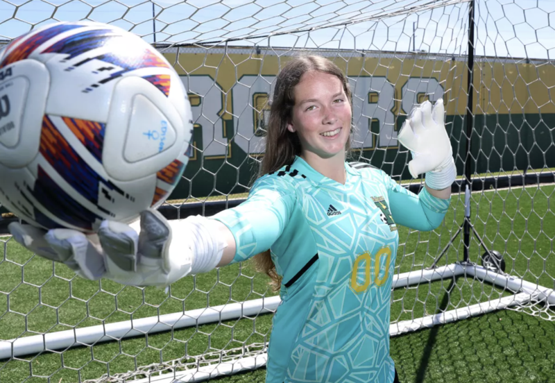 Tatum Trout stands in front of a soccer goal while holding out a soccer ball