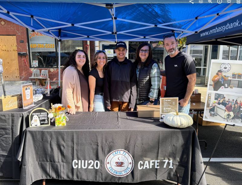student and staff in front of colonial cafe 71 coffee tent