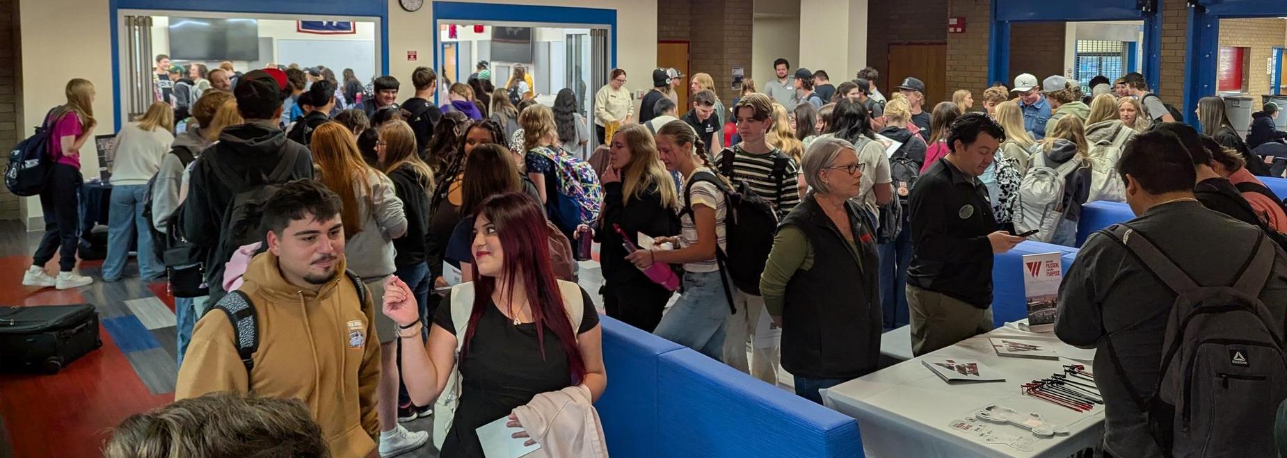 Crowd of students gathering in a lobby with tables and a large banner overhead.