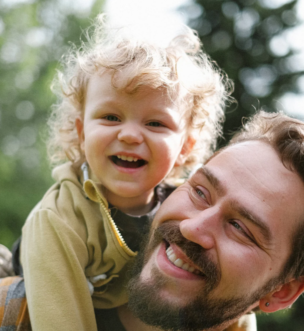 A smiling man holds a joyful child on his back outdoors.