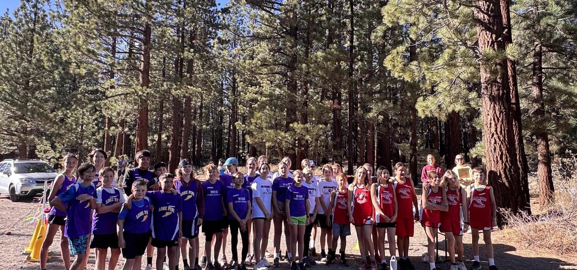 A large group of children in purple and red jerseys standing among trees in a forest.