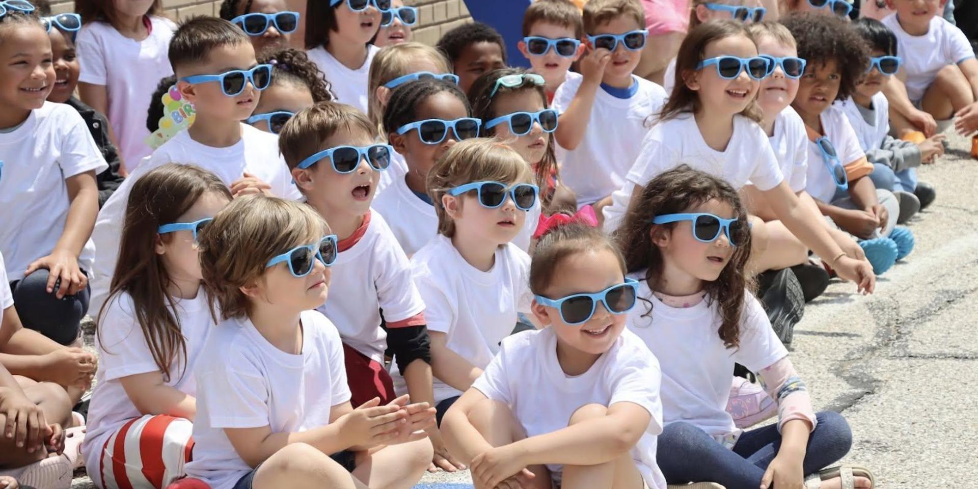 Children wearing sunglasses, smiling and enjoying an outdoor event.