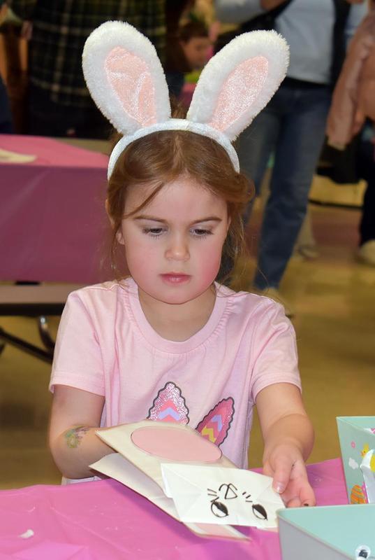 Girl with bunny ears crafts a card at a table with a pink tablecloth.