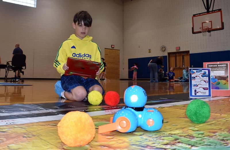 Child in a yellow hoodie interacts with colorful learning tools on the floor.