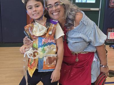 Child and adult smiling together, wearing costumes made of snack wrappers.