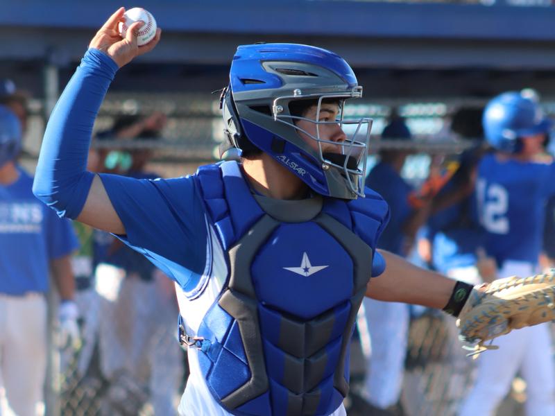 Baseball catcher in gear ready for play amidst teammates in background.