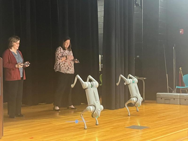 Educators standing on a stage demonstrating robot dogs.