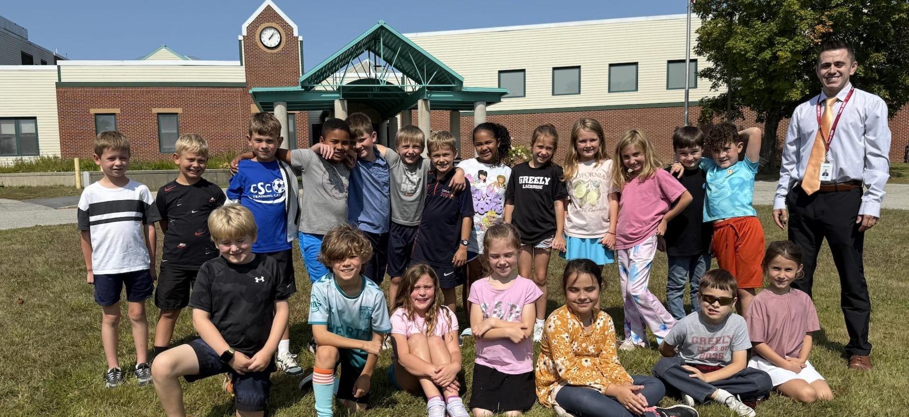 A group of students and a teacher posing outside a school building on a sunny day.