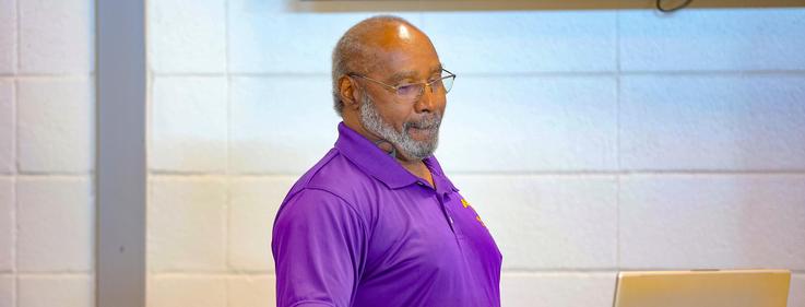 A man in a purple polo shirt giving a presentation at a podium.